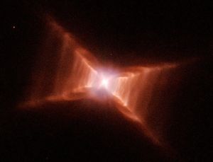 A glowing star at the center of what looks like a red X. Closer to the center, red-orange rectangular clouds of gas and dust are thicker., thinning out before reaching the "ends" of the X.