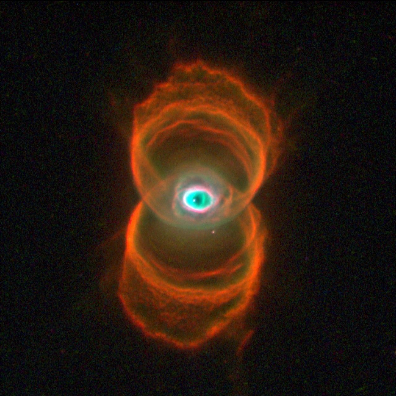 Two sets of rings in orange and gold stacked one above the other form the shape of a hourglass. At image center, where the two sets of rings overlap, is an area of white, green and black dust in a shape that is similar to the human eye.