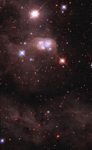 Pale red streaks of dust cross the bottom of the image. Near the top are several bright stars and a white-orange double-bubble of gas surrounded by more reddish dust.