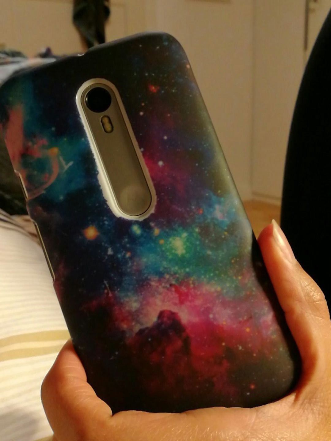 In their left hand, a person holds a smart phone facing away from the camera. The back of the phone's cover has a beautiful image of a colorful nebula with a smattering of bright stars in the center.
