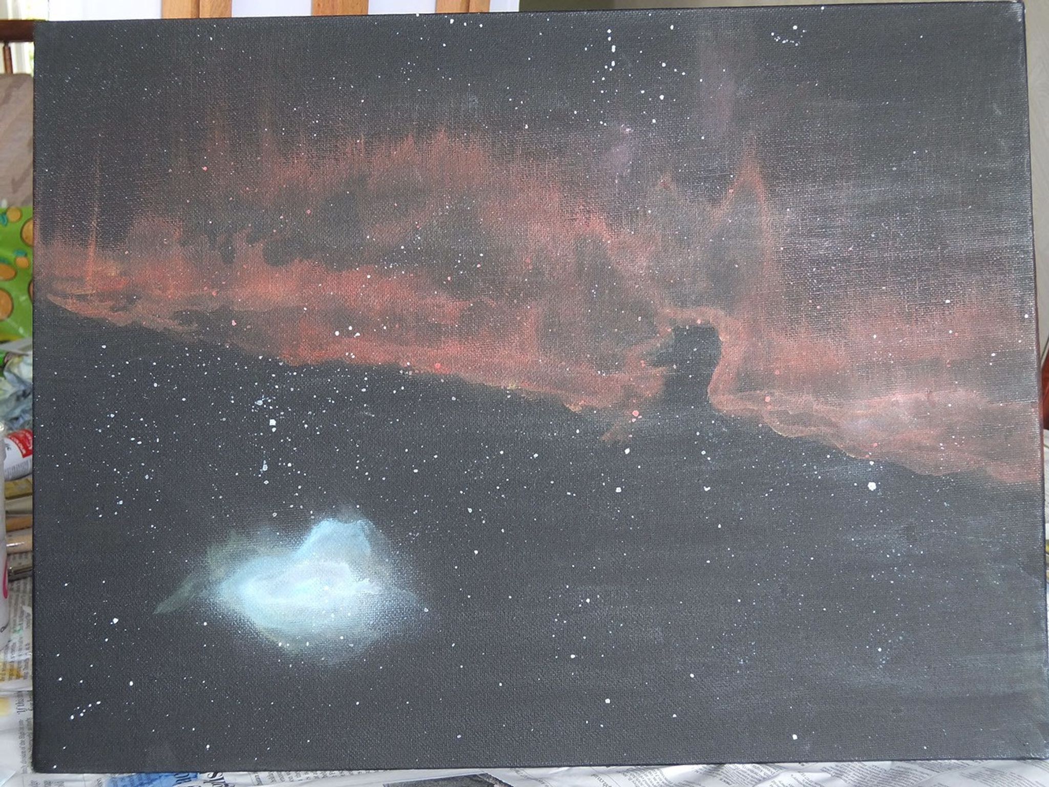 A painting of the Horse Head Nebula on an acrylic board. The board is painted black, with numerous small white dots to represent stars, a bluish-white cloud of gas in the lower left, and a large streak of reddish-brown gas and dust across the whole board.