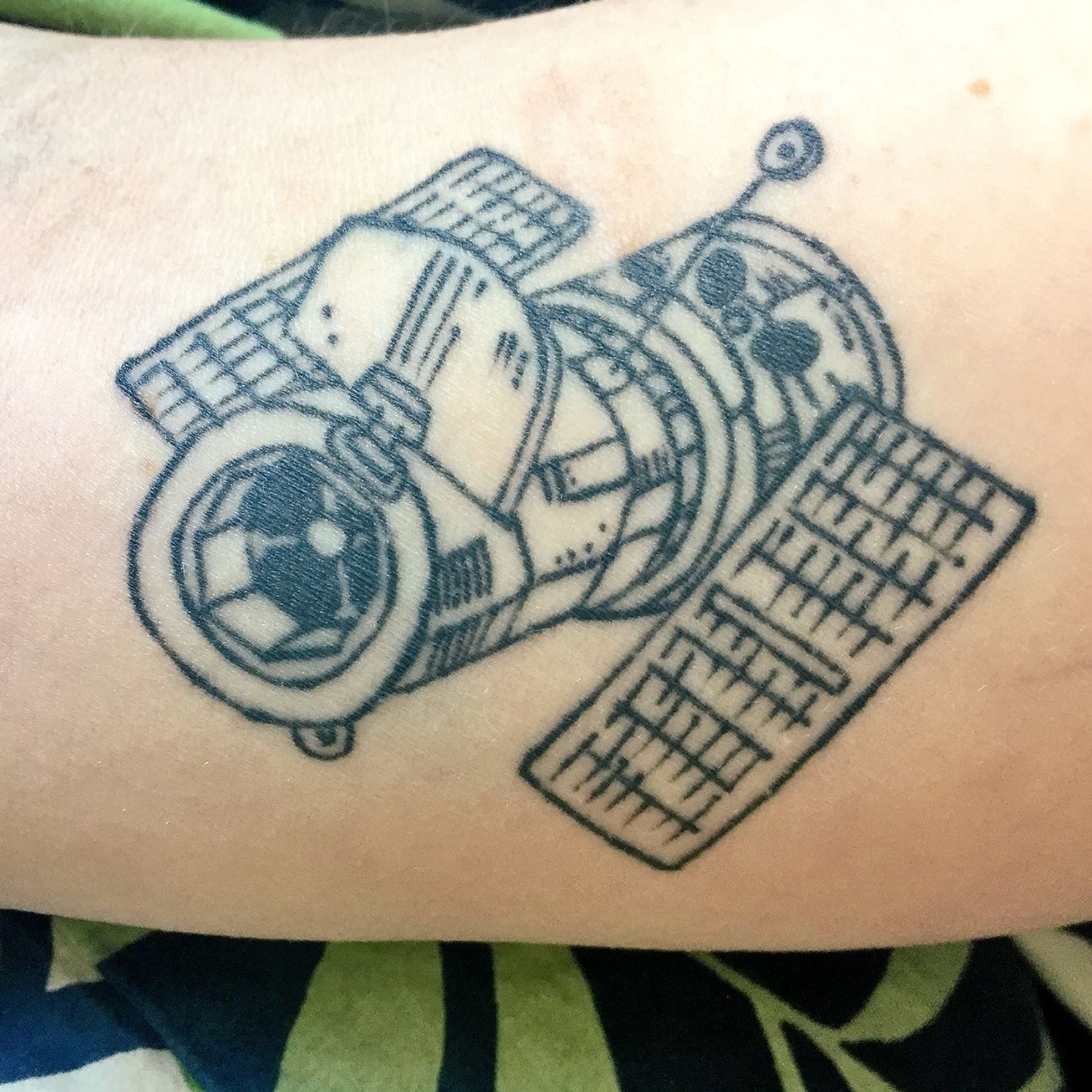 A person has a fairly detailed tattoo of the Hubble Space Telescope in black ink on their arm.