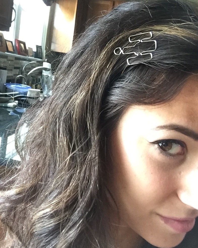A young woman photographs her face at an angle (with only one eye visible) to show the silver Hubble-shaped paperclip that she's wearing in her dark hair like a barrette.
