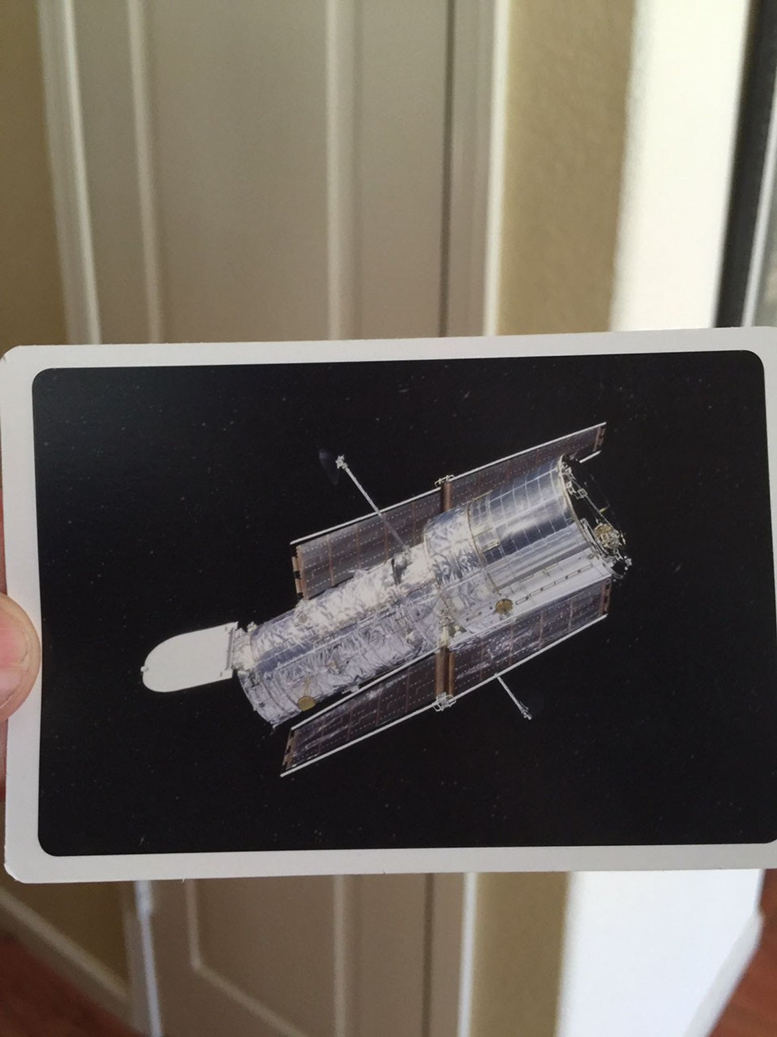 A person holds up a flash card with a real photo of the Hubble Space Telescope against the black backdrop of space.