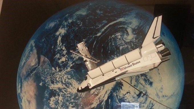 A model of Space Shuttle Discovery with a model of the Hubble Space Telescope, suspended in front of a large image/model of the Earth.