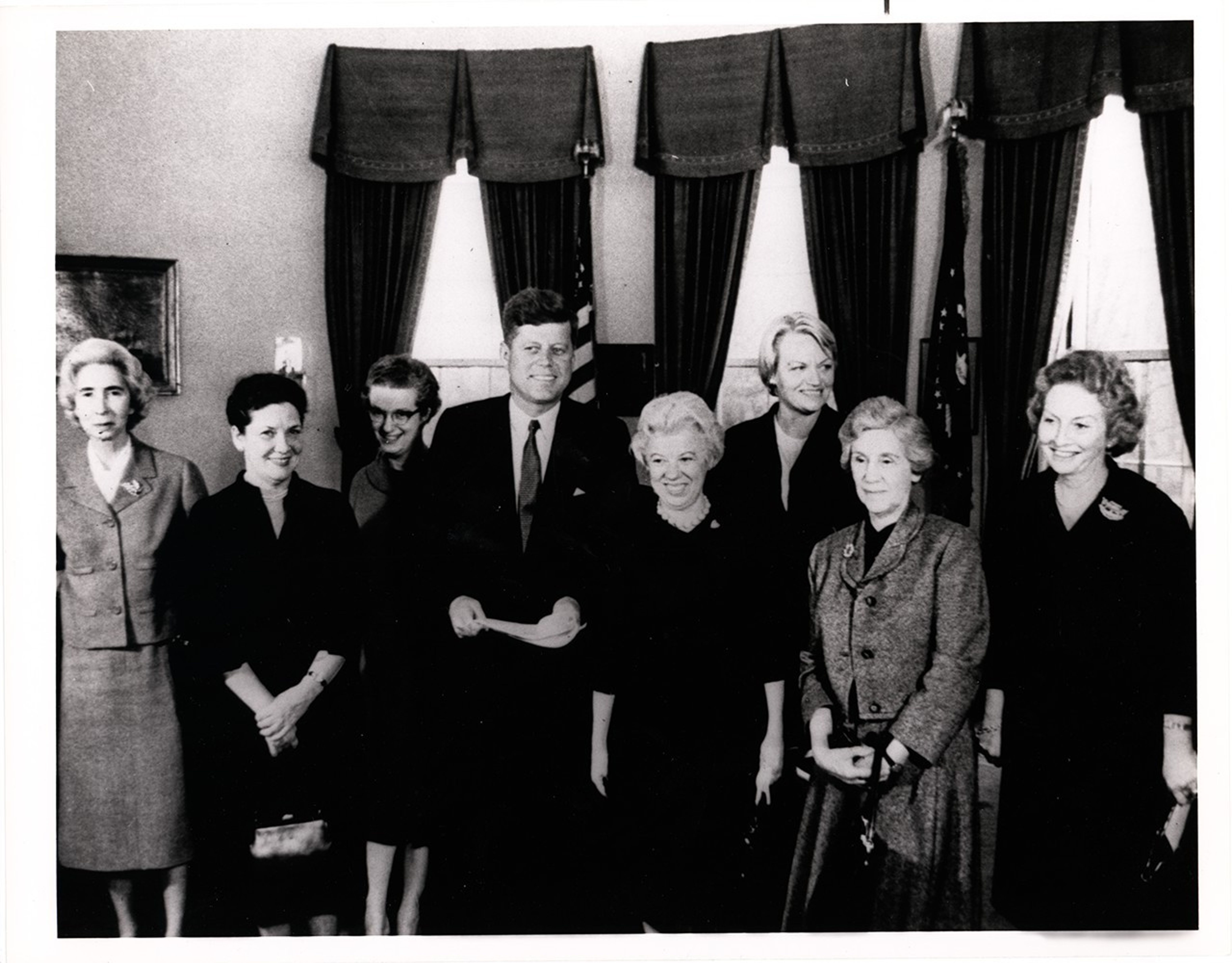 Nancy Grace Roman with President John F. Kennedy and six other women in the Oval Office. Roman is the third from the left, standing next to Kennedy.