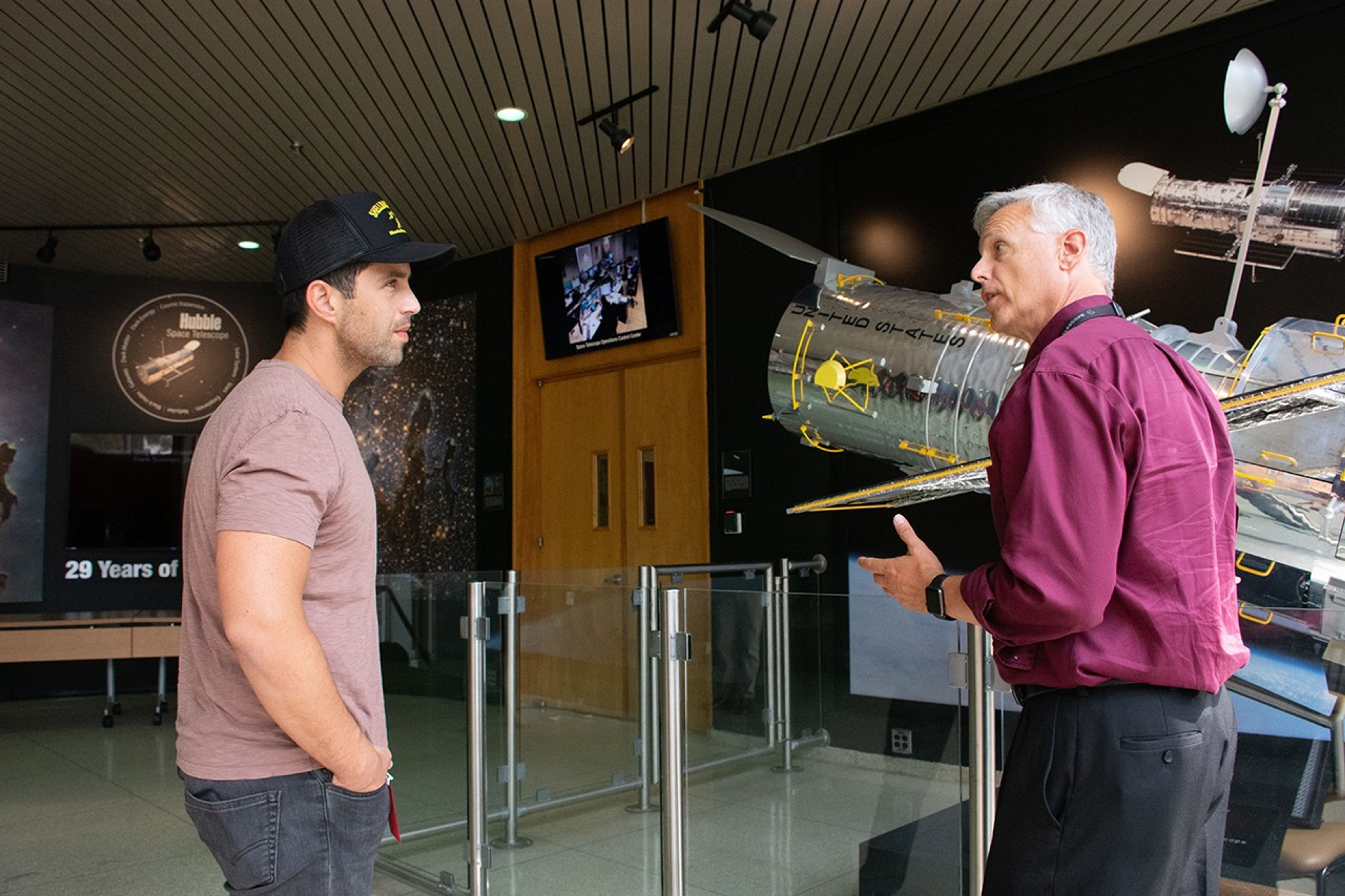 Jim Jeletic, right, gestures to the model of Hubble behind him while speaking to the listening Josh Peck, left.