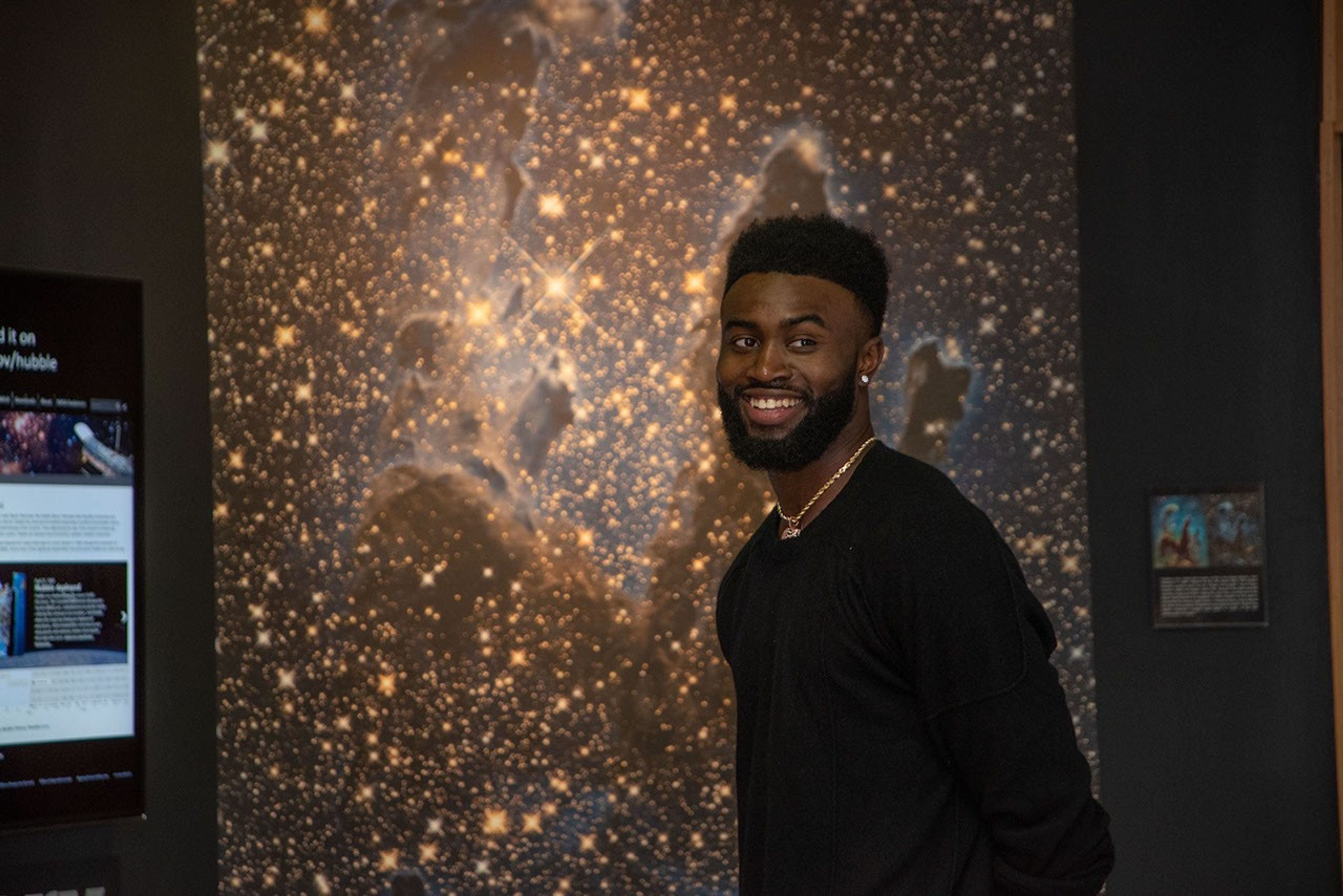 Brown smiles in the direction of the camera, with a large infrared image of the Eagles of Nebula on the wall behind him.