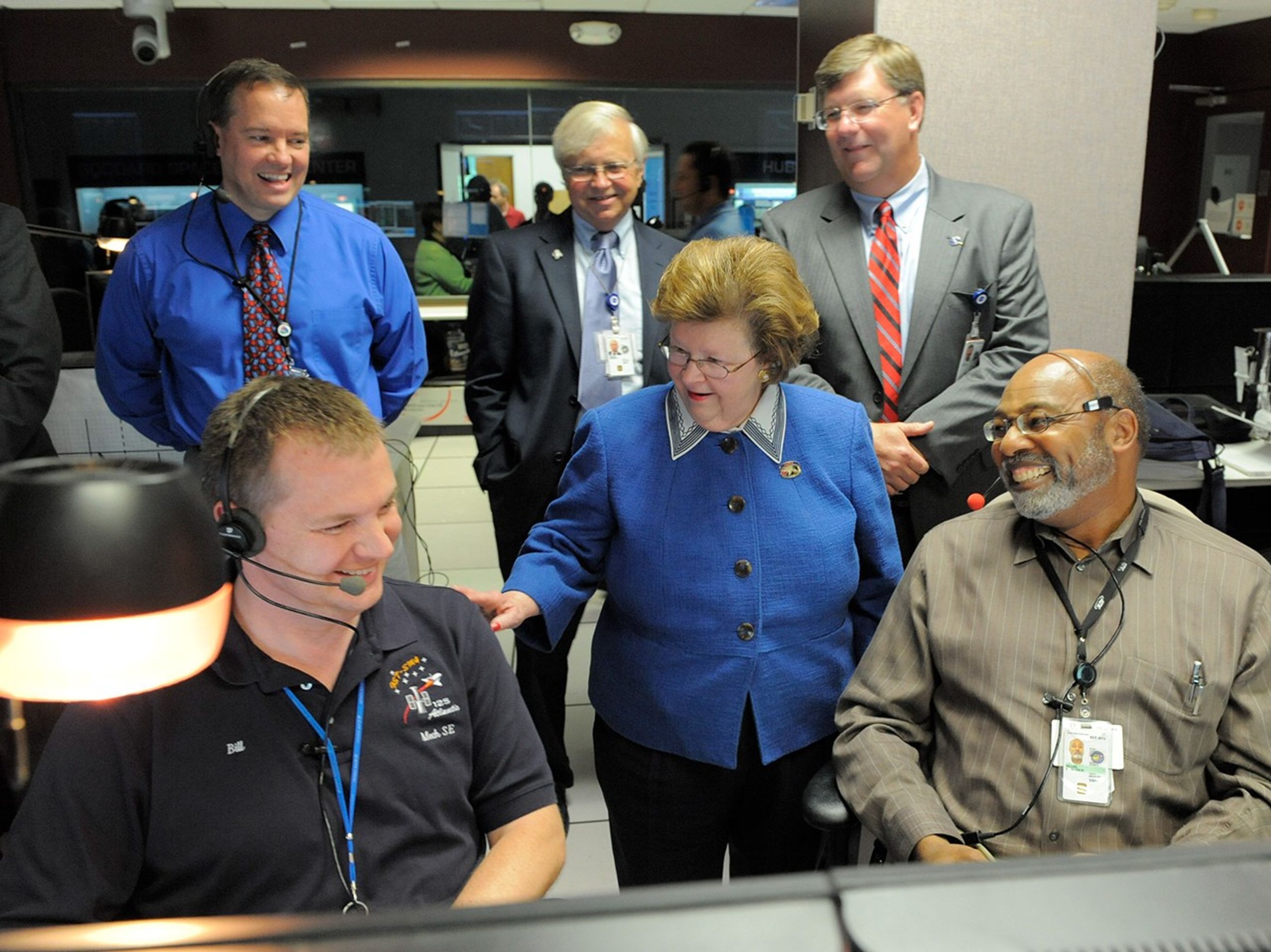 Mikulski, center, stands between a smiling Miller and Nilsson while putting a hand on the latter's shoulder. Behind her, three more gentlemen watch with a smile.