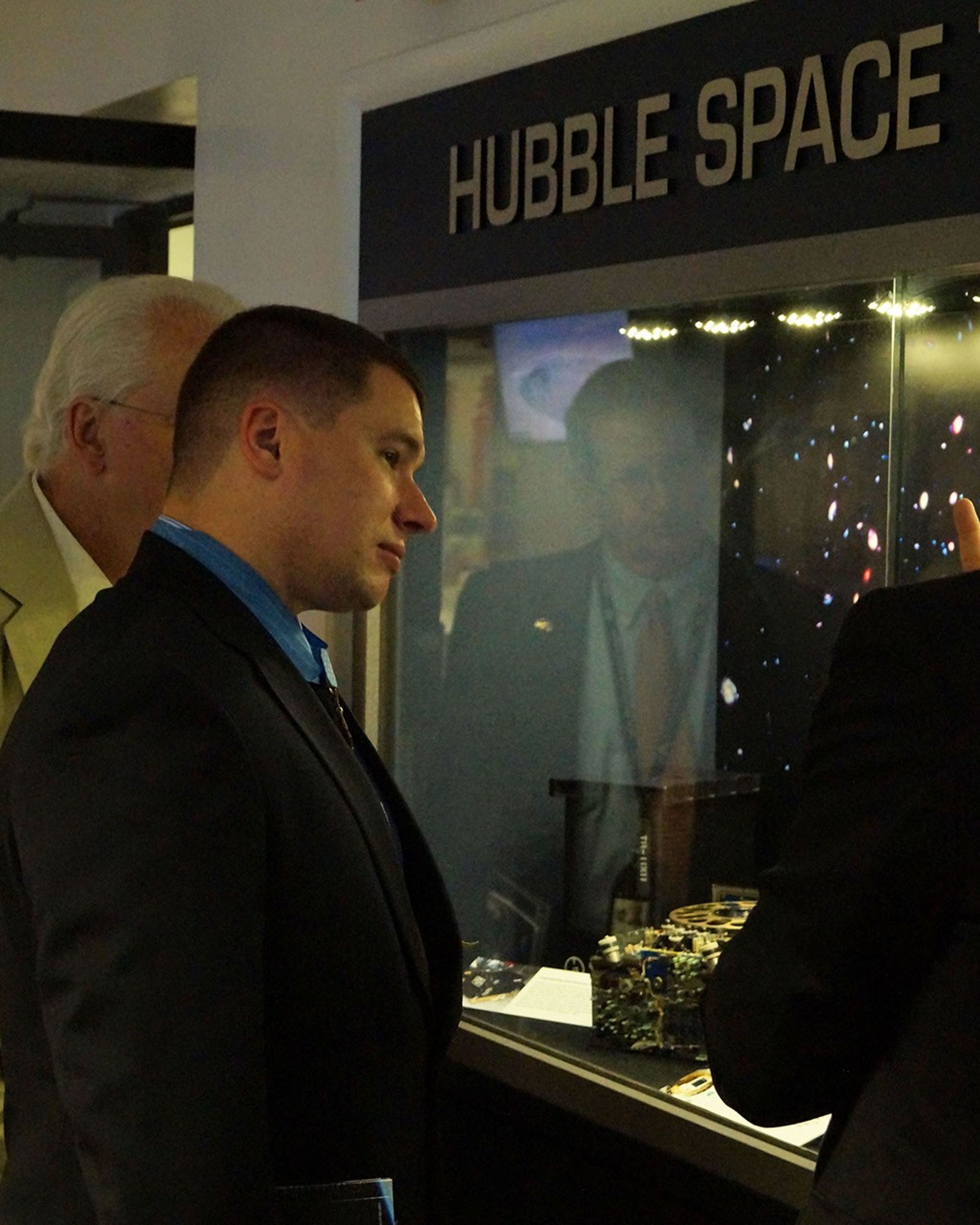 White, center, looks into the Hubble display case at the instruments, while two others are partially visible on the left and right.