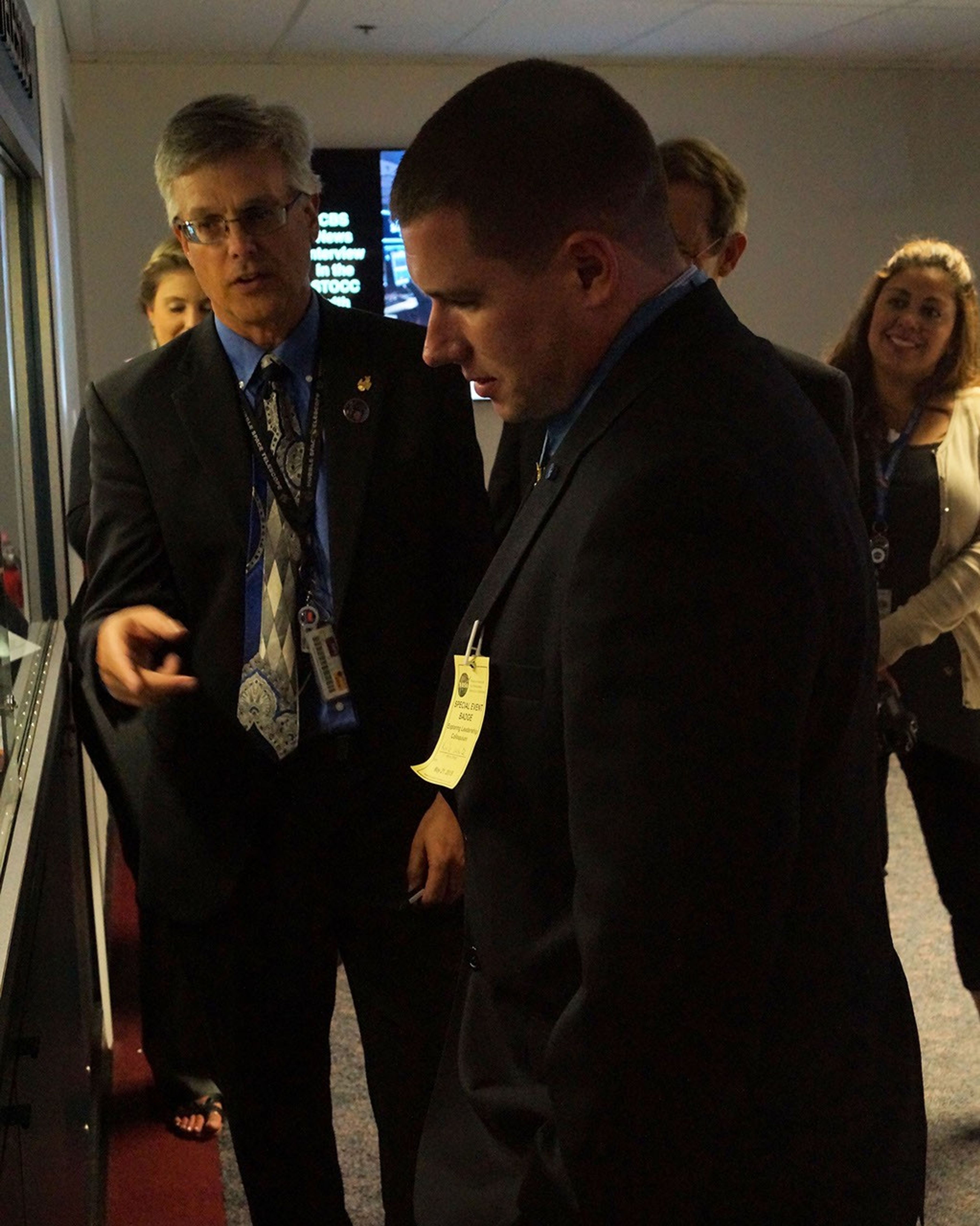Jeletic, left, points at the display case while speaking to White, right, who's looking into the case. Three more men and women are partially visible in the background, watching.