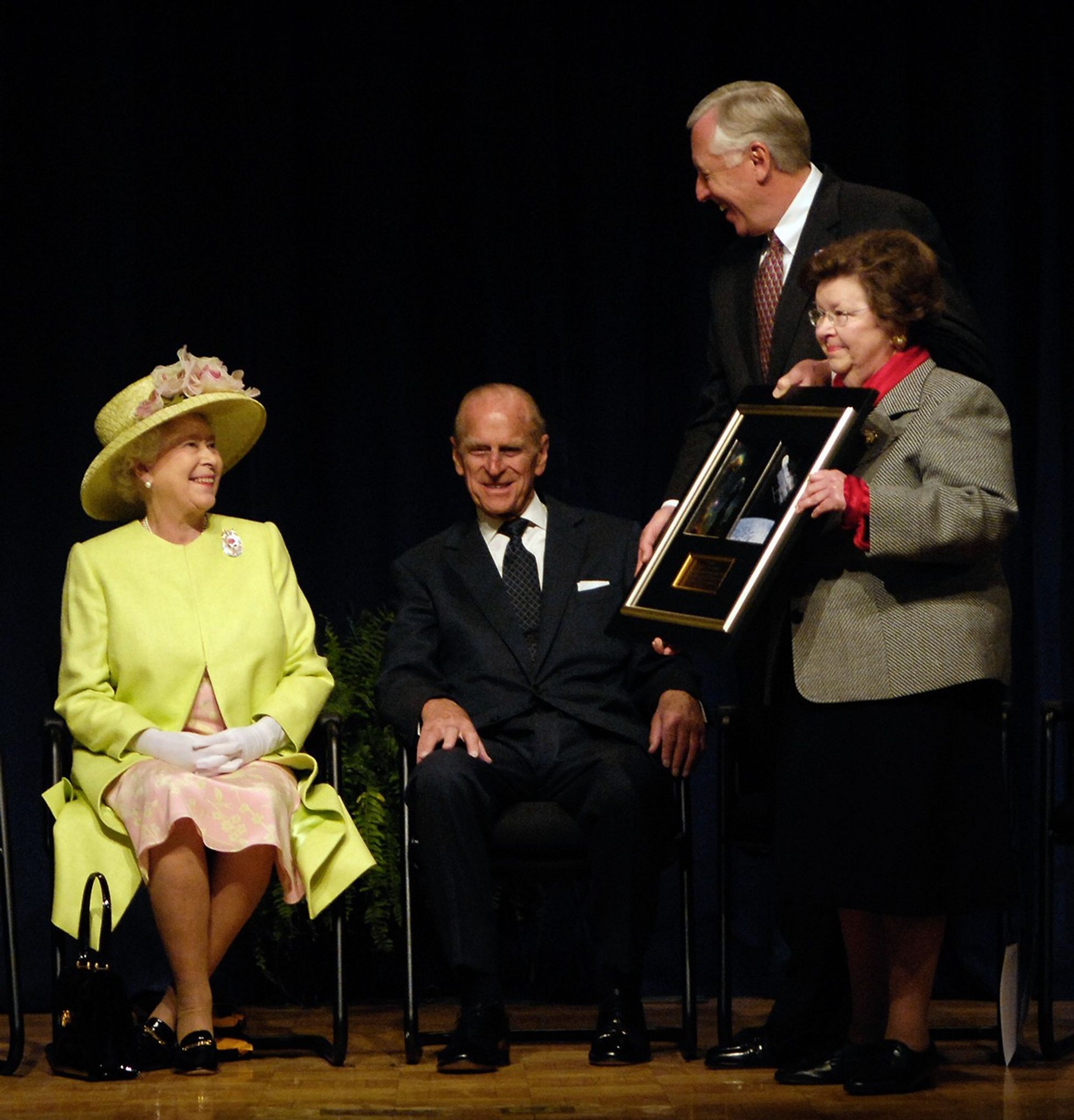 Queen Elizabeth II (far left) and Prince Philip (center left) sit while Rep. Hoyer and Sen. Barbara Mikulski (right) hold a framed picture of Hubble and the Eagle Nebula to give to them.