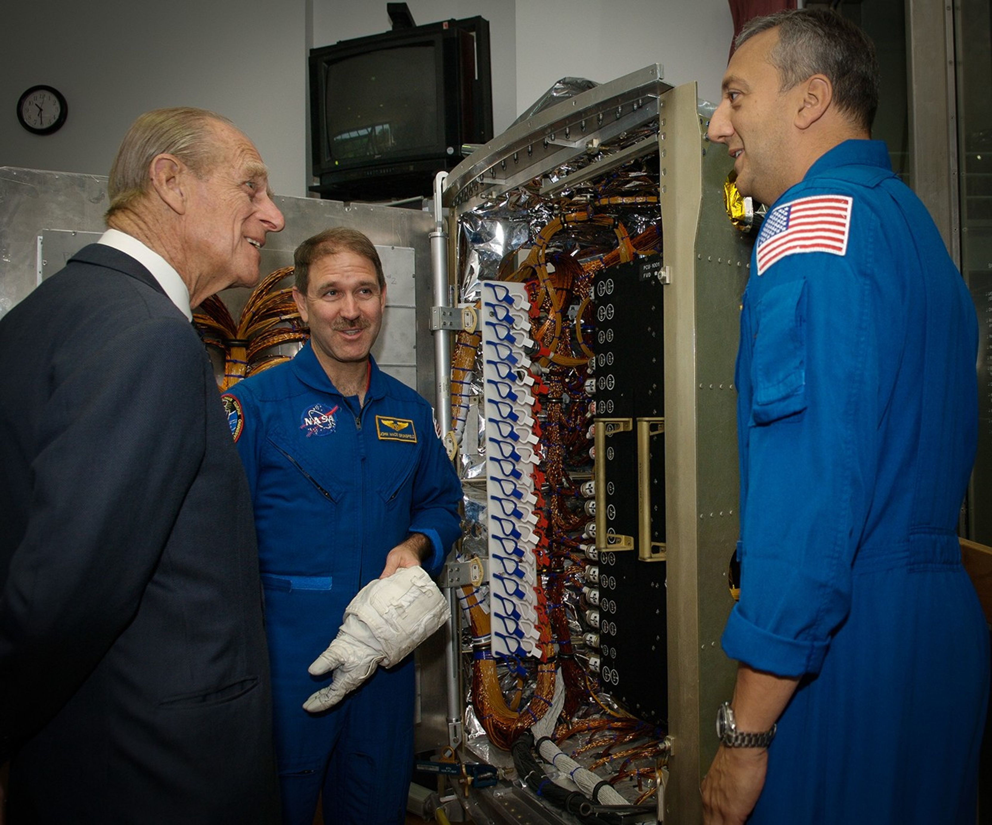 Astronauts Massimino (right) and Grunsfeld (center) present the Power Control Unit training similuator, a large cabinet full of wires and knobs of various colors, to Prince Philip (left).