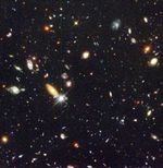 On a grainy black background, dozens of galaxies of various shapes, sizes, and colors are scattered.
