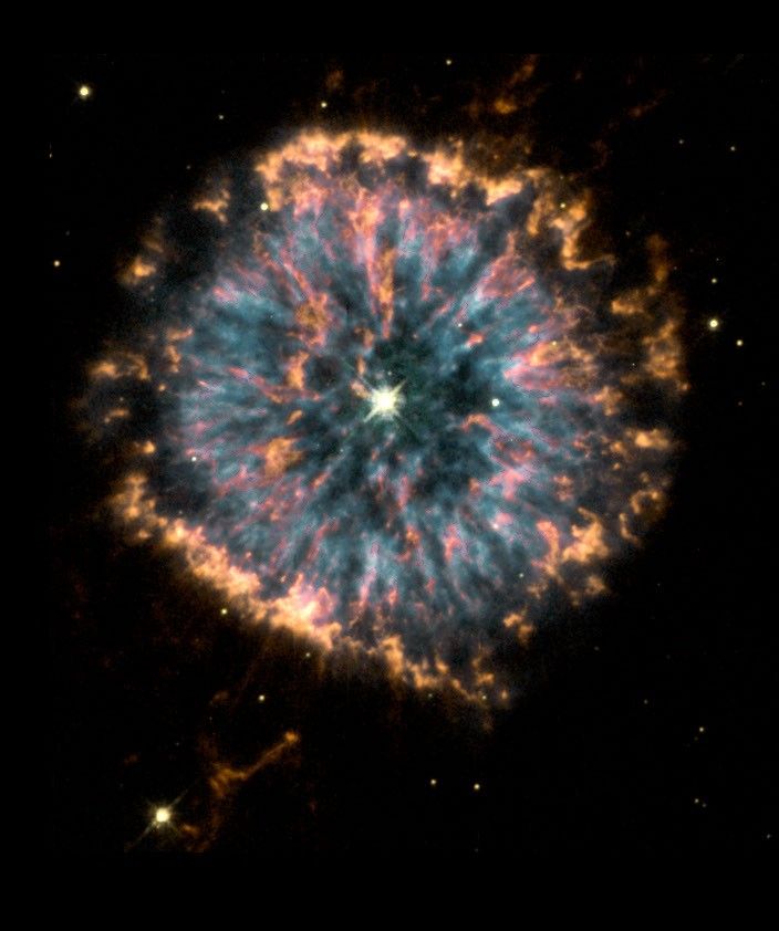A cloud of gas and dust resembling an eye. The outer edges of the eye are pale orange; the "iris" is blue, orange, and pink; and the center "pupil" is darker and contains a glowing star. The background is black, with faint stars in the background and wisps of orange gas.