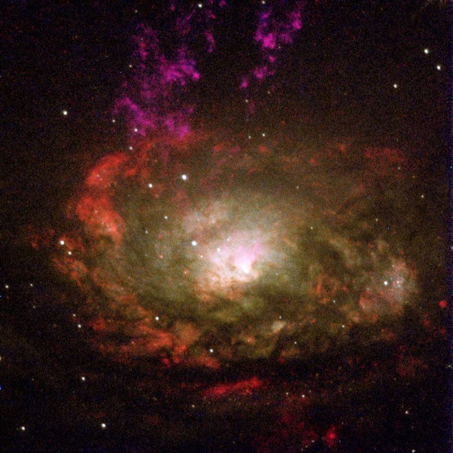 A spiral galaxy that is white in its center and red at its edges. Purple gas rises up and out of the white center in the shape of a "V."