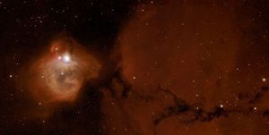 In the right half of the image, dark red gas forms a background haze, streaked with a line of black dust. On the left, a bright white star glows near the top of a red-and-orange bubble of gas and dust.