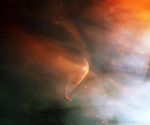 A very small portion of a larger nebula with a distinct arc of yellow-orange and more diffuse orange gas streaming away to its upper left.