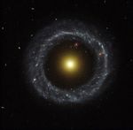 A large ring of circular blue stars surrounds a bright, large yellow nucleus, with a large gap between the ring and the nucleus.