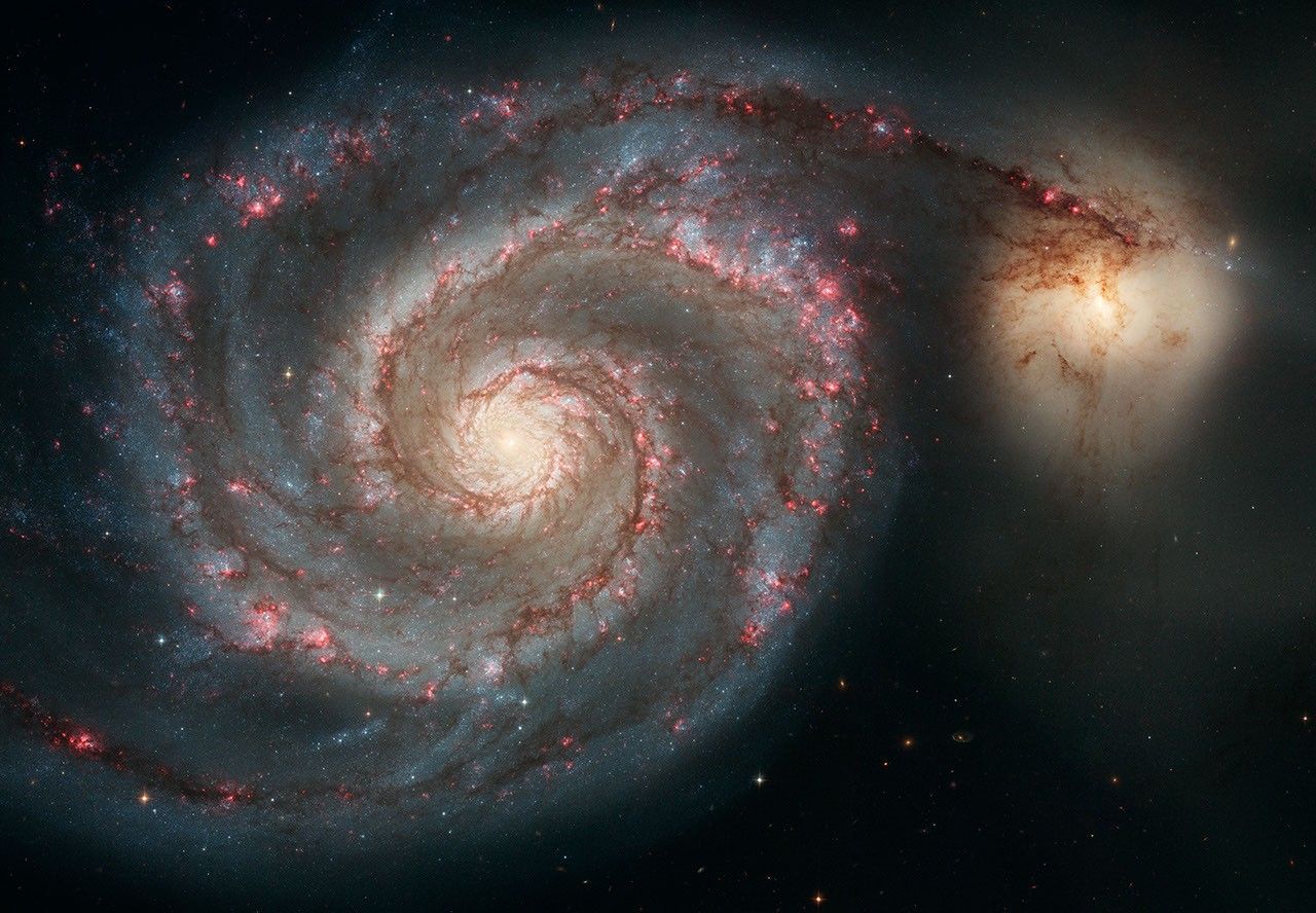 Large colorful spiral galaxy interacting with a small companion galaxy.