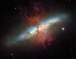Hourglass-shaped red plumes of gas are shooting outward from above and below a bright blue, disk-shaped center of a galaxy.