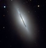 An edge-on spiral galaxy with a thin, clumpy line of dust stretches from upper left to lower right.