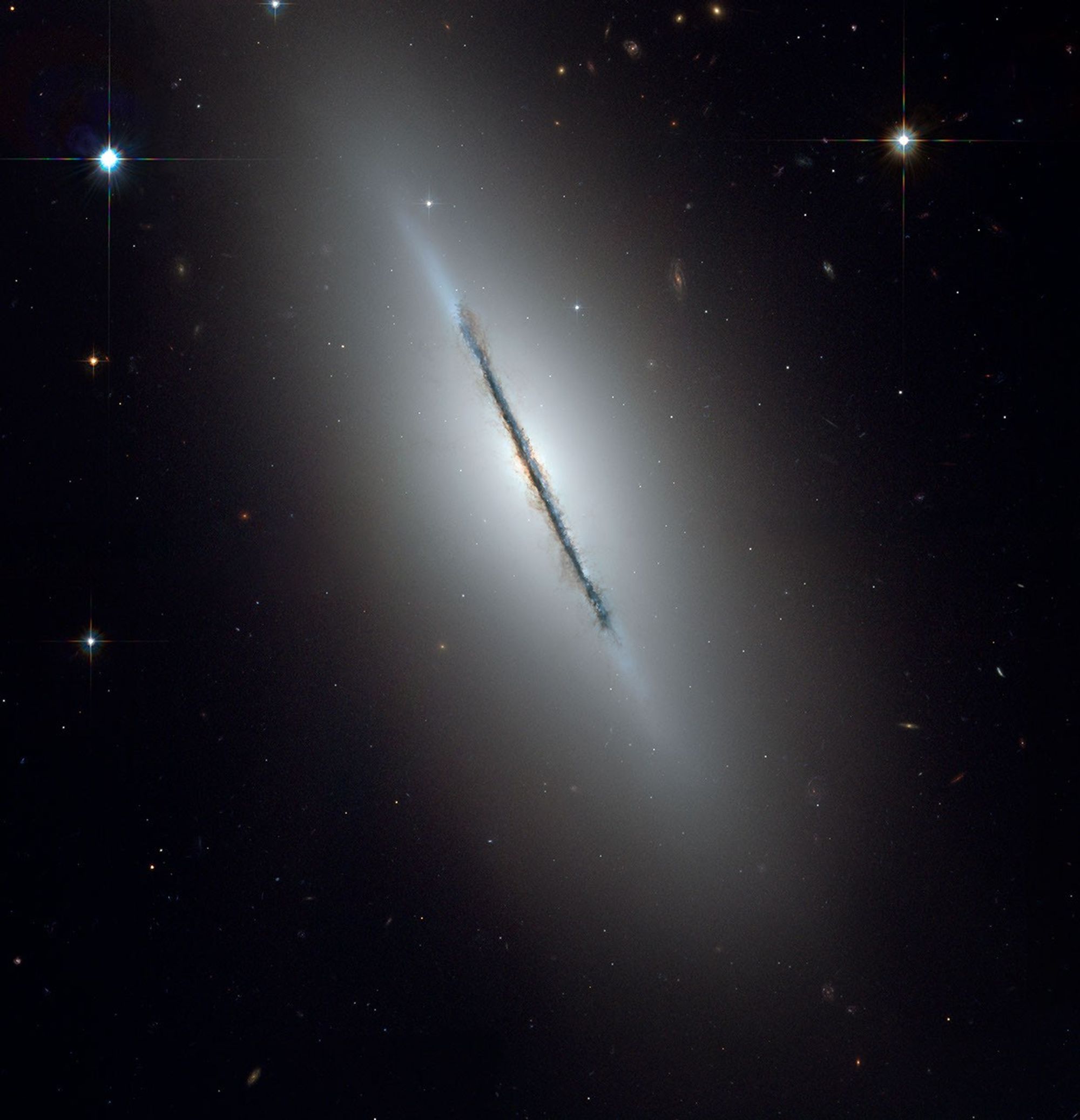 An edge-on spiral galaxy with a thin, clumpy line of dust stretches from upper left to lower right.