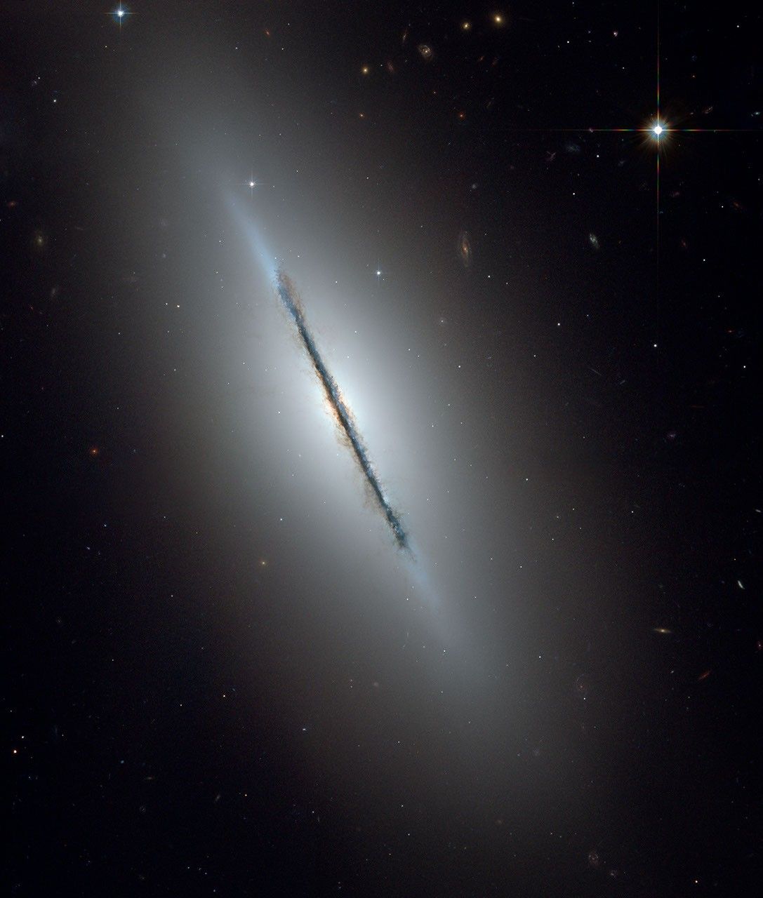 An edge-on spiral galaxy with a thin, clumpy line of dust stretches from upper left to lower right.