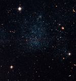 A field of blue, white, and red stars and galaxies against the black background of space. There is an irregular, denser grouping of stars in the center.
