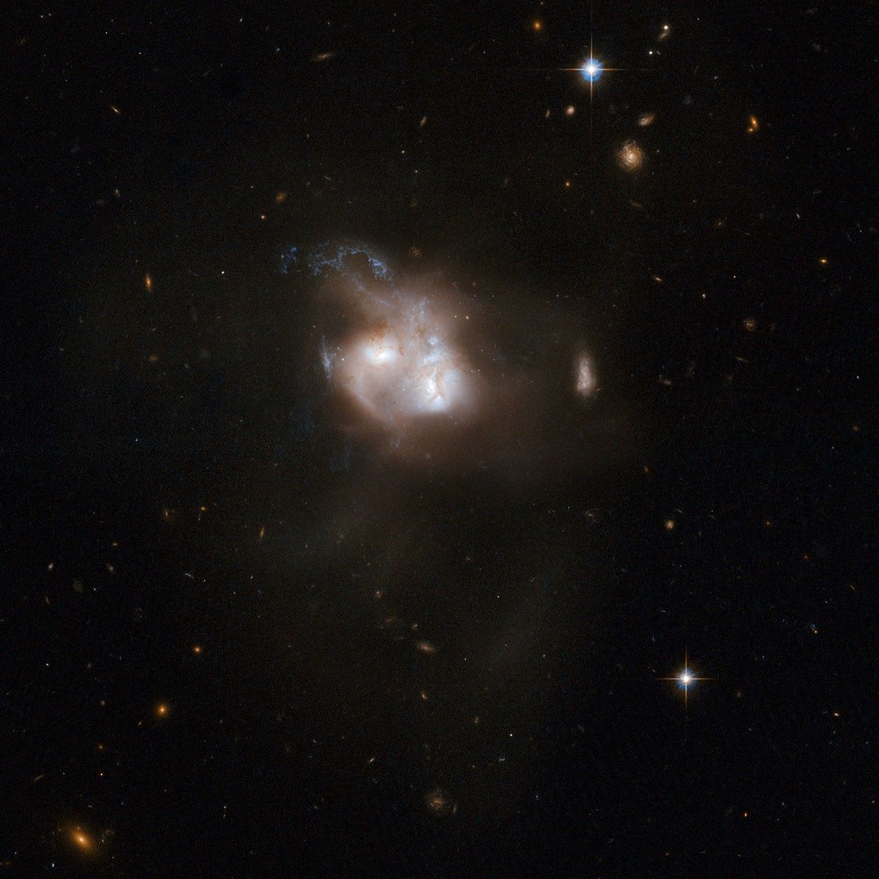 Two interacting galaxies with white centers are almost overlapping. The white, red, and blue plumes of gas that surrounds the galaxies’ centers are interacting with each other as they merge.