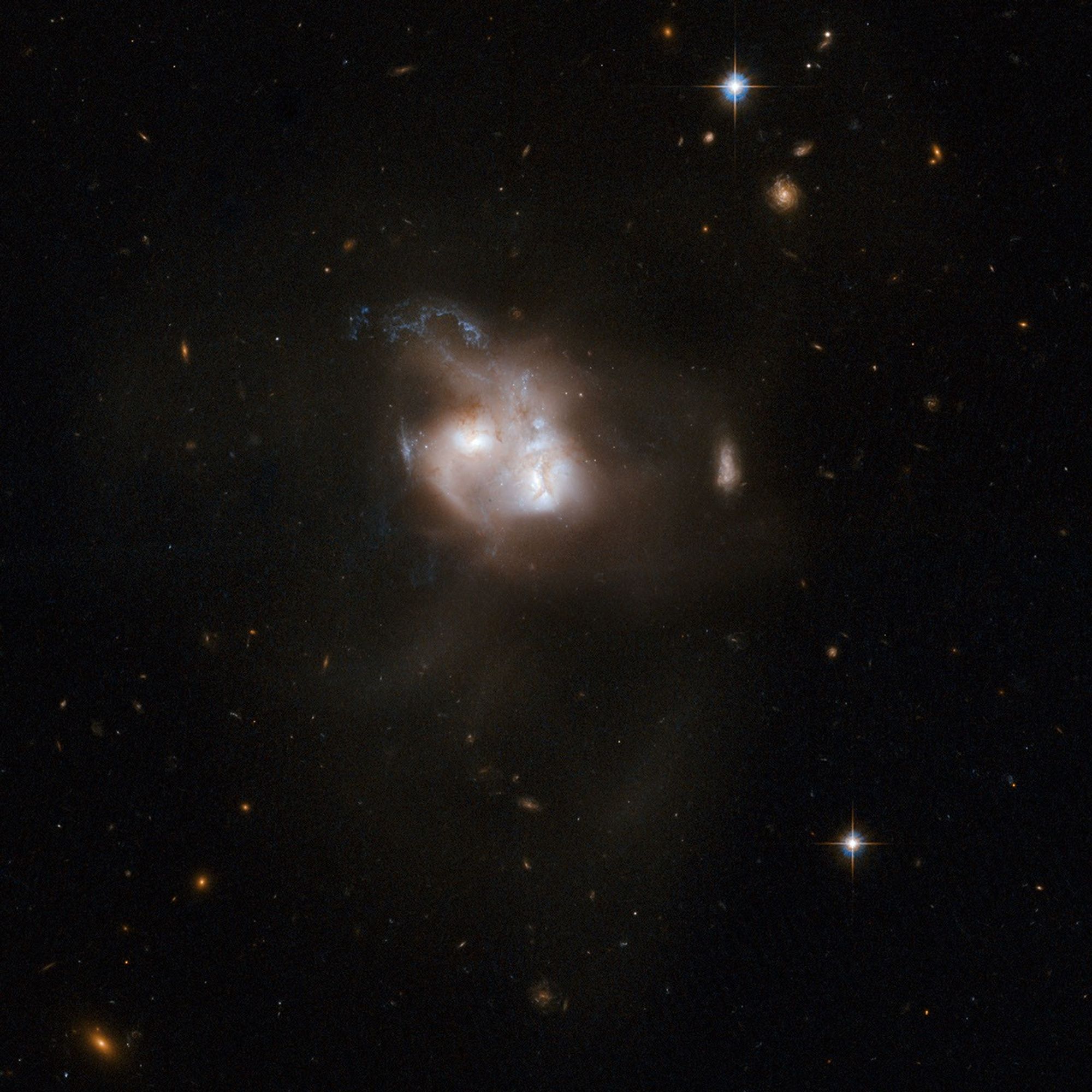 Two interacting galaxies with white centers are almost overlapping. The white, red, and blue plumes of gas that surrounds the galaxies’ centers are interacting with each other as they merge.