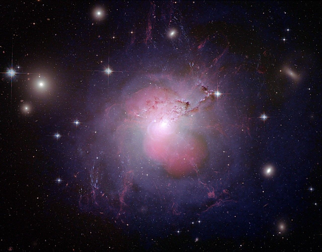 A galaxy with a white center surrounded by pink lobes above and below it. Outside the pink lobes is a violet shell that surrounds the galaxy. From the center of the galaxy are stringy filaments of red gas.