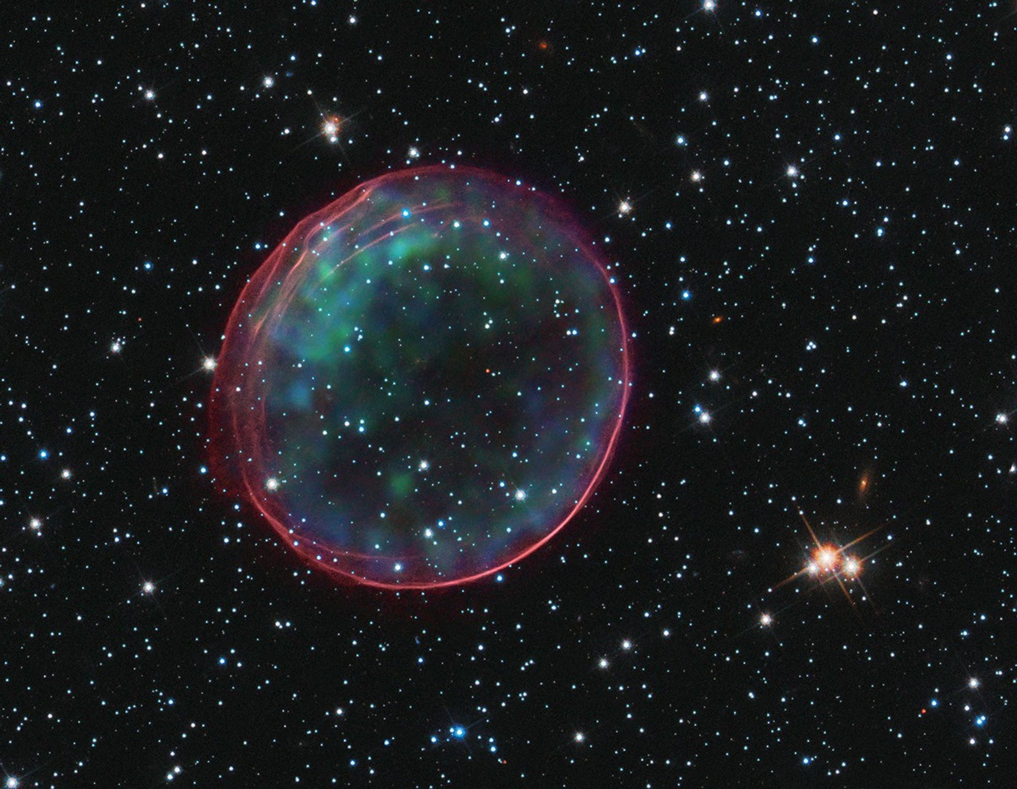Supernova remnant resembling a bubble. Its exterior is tinged with red, while its interior has blue-green blotches.