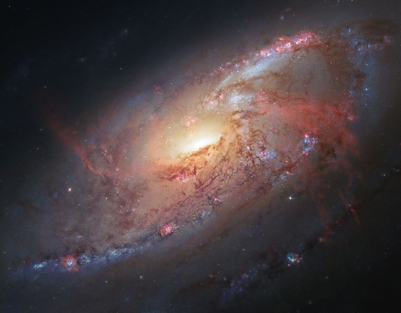 A galaxy with red and blue spiral arms stretching clockwise around its bright yellow-white core.