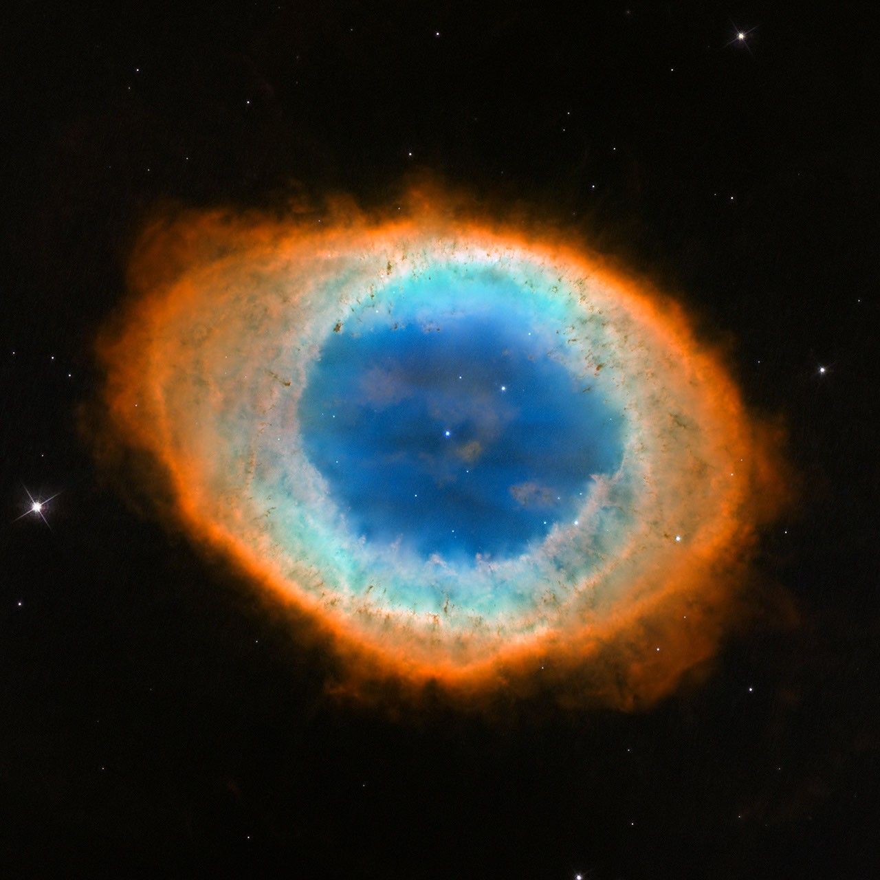 The Ring Nebula is a large, semi-transparent circle with several layers around it that appear like a misshapen football slightly angled from top left to bottom right.