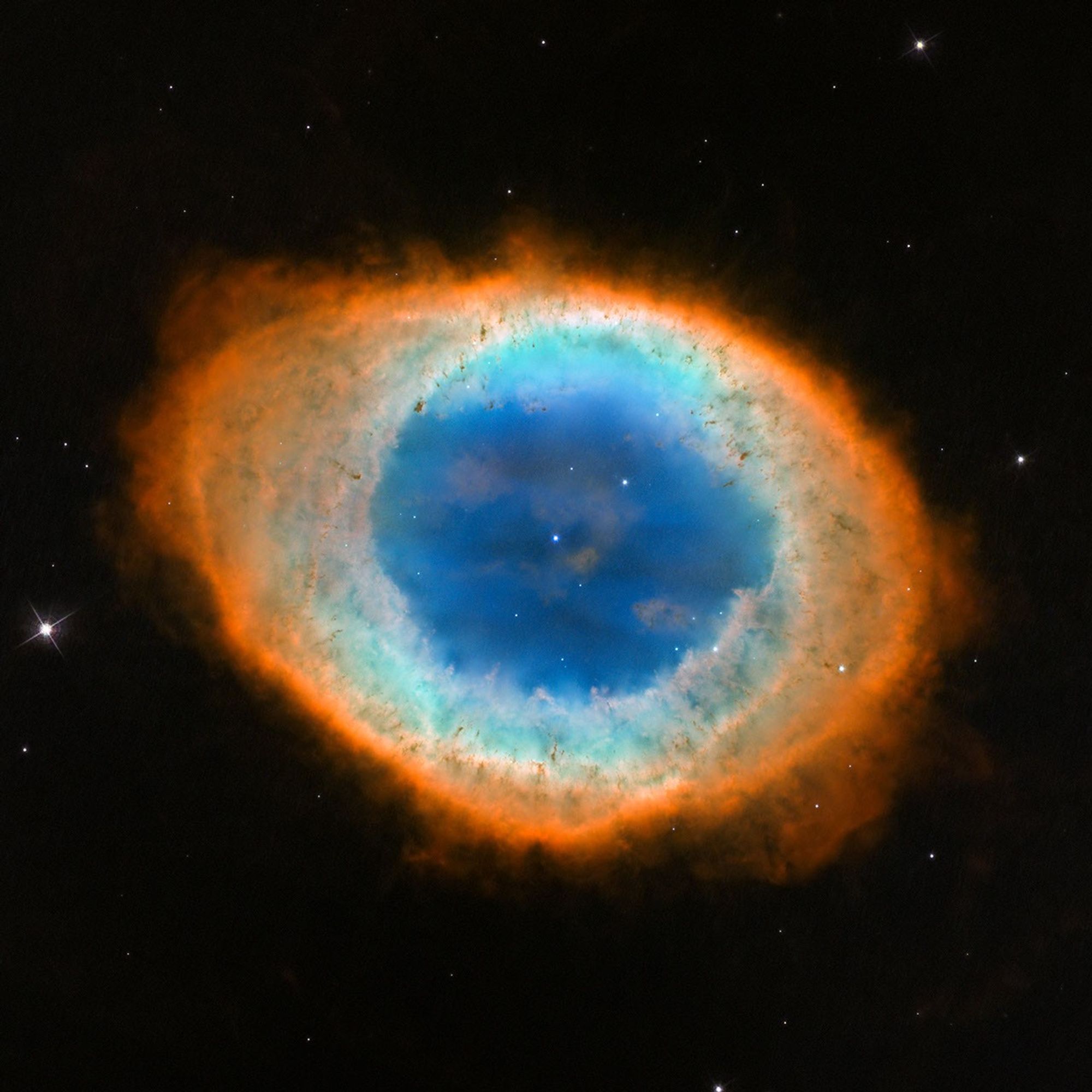 The Ring Nebula is a large, semi-transparent circle with several layers around it that appear like a misshapen football slightly angled from top left to bottom right.