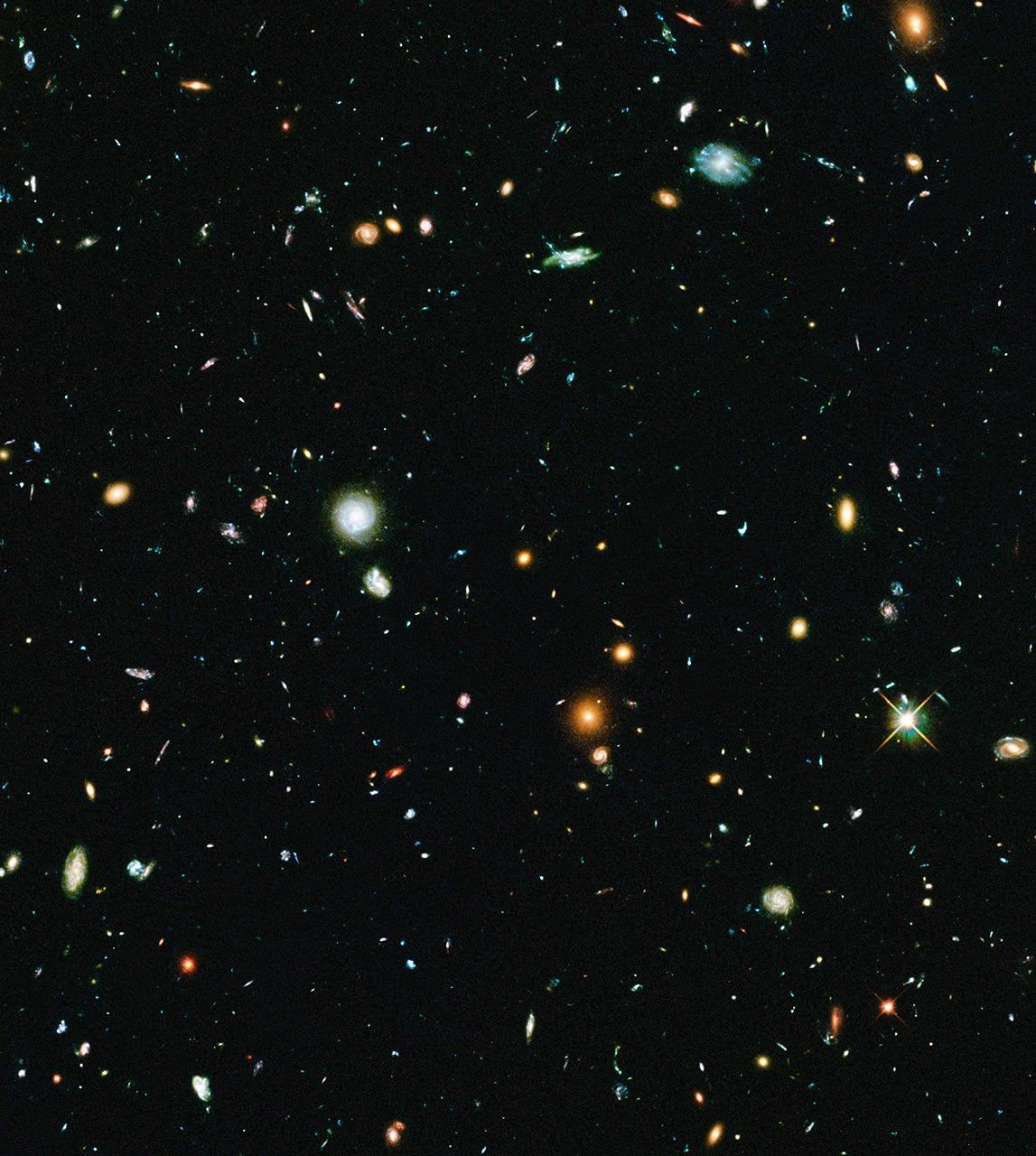 Hundreds of galaxies in a diverse array of shapes and colors are scattered across the dark background of space.