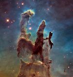 The Pillars of Creation. Three dark brown columns of gas and dust illuminated by starlight.