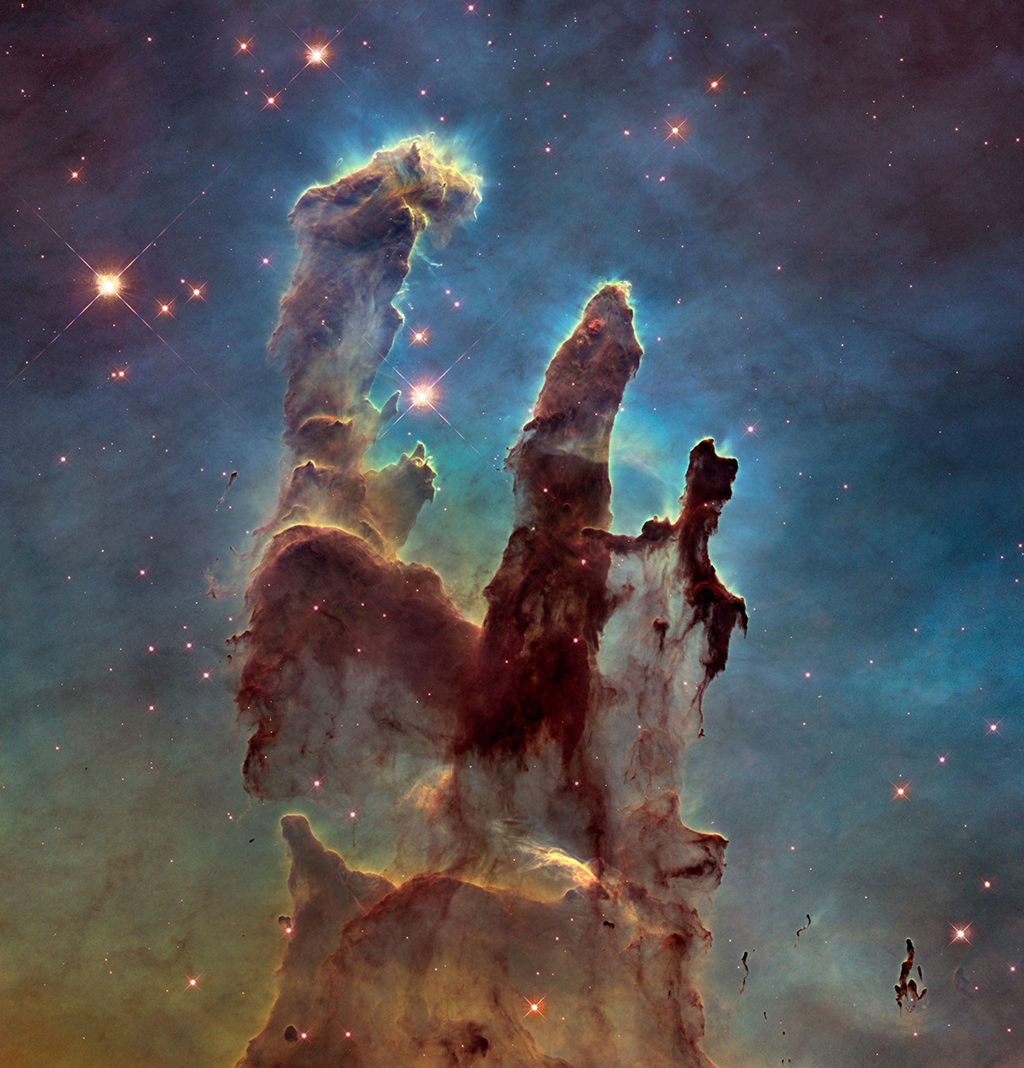 The Pillars of Creation. Three dark brown columns of gas and dust illuminated by starlight.