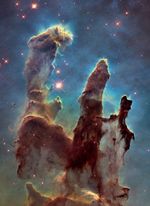 The Pillars of Creation. Three dark brown columns of gas and dust illuminated by starlight.