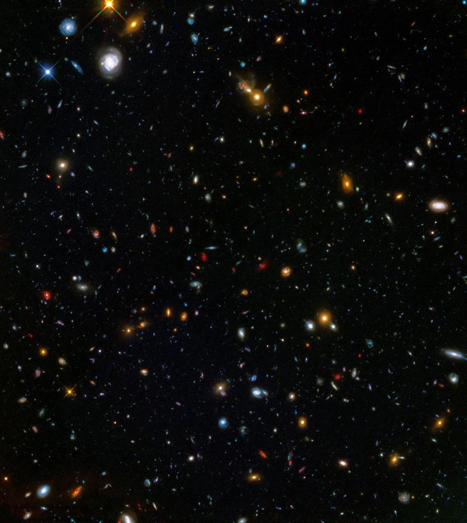 Thousands of galaxies appear all across the view. A trio of spiral galaxies and a couple of bright stars appear in the upper-left corner.