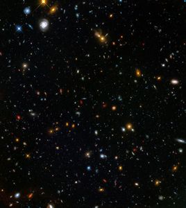 Thousands of galaxies appear all across the view. A trio of spiral galaxies and a couple of bright stars appear in the upper-left corner.