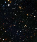 Hundreds of galaxies of various colors and sizes are scattered across the view, and about a dozen curved or wavy white streaks appear in random locations.