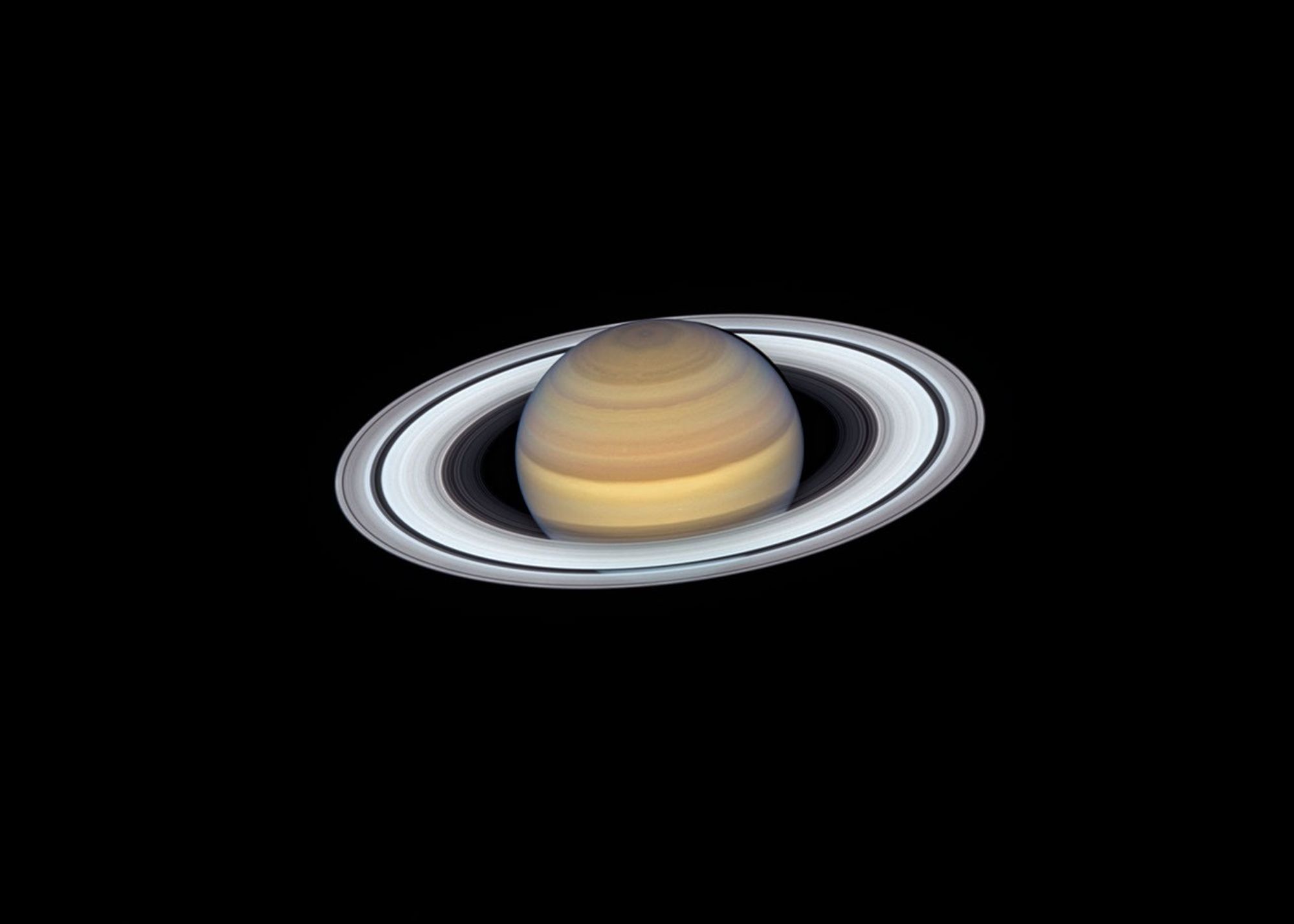 A view of Saturn from the Hubble Space Telescope captures exquisite details of the ring system, which looks like a white phonograph record with grooves that represent detailed structure within the rings.