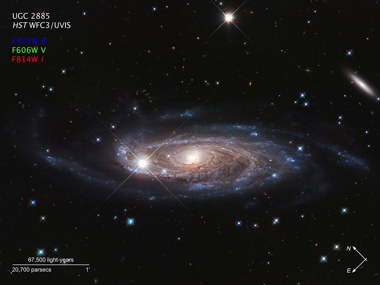 Spiral galaxy with sweeping spiral arms on a dark background with compass arrows, scale bar, and color key for reference.