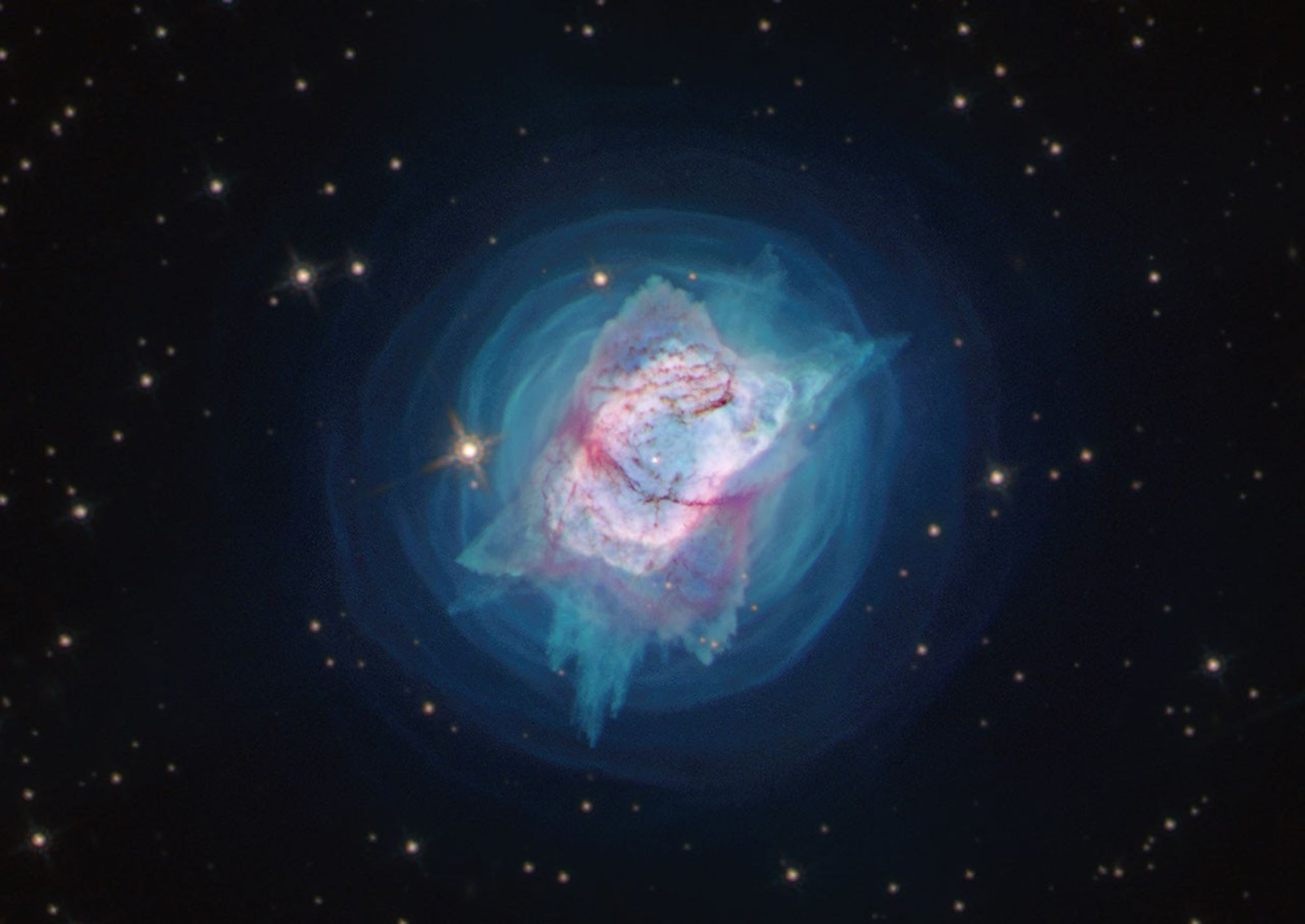 A nebula with a pink elliptical shell is surrounded by concentric rings of blue gas, all set on a black star-filled background.