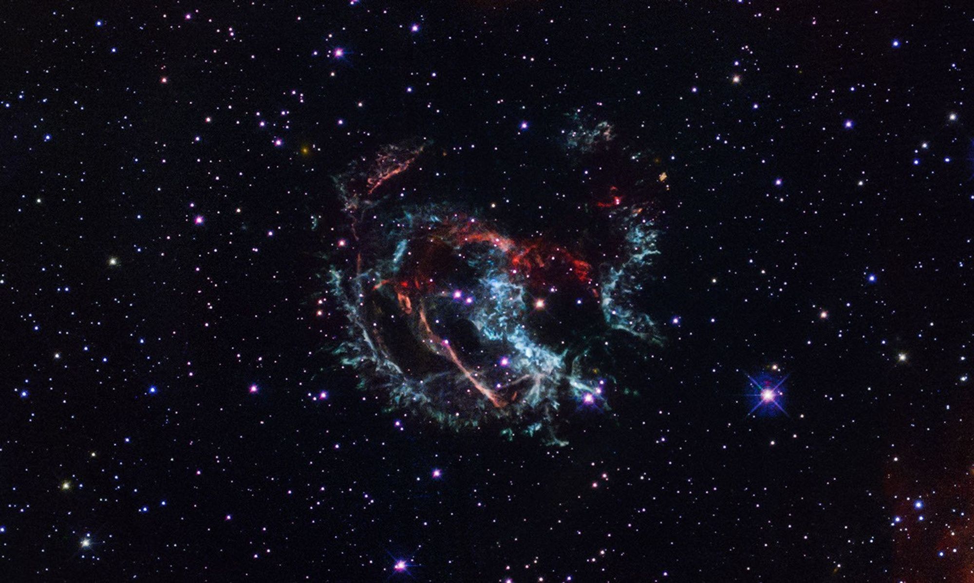 Plumes of gas that are colored blue, red, and green form a loose circle at the center.