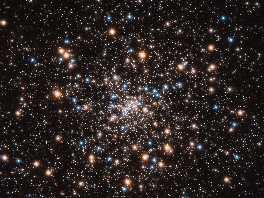 Image of globular star cluster NGC 6397 containing blue stars, red giant stars, and a number of small white objects