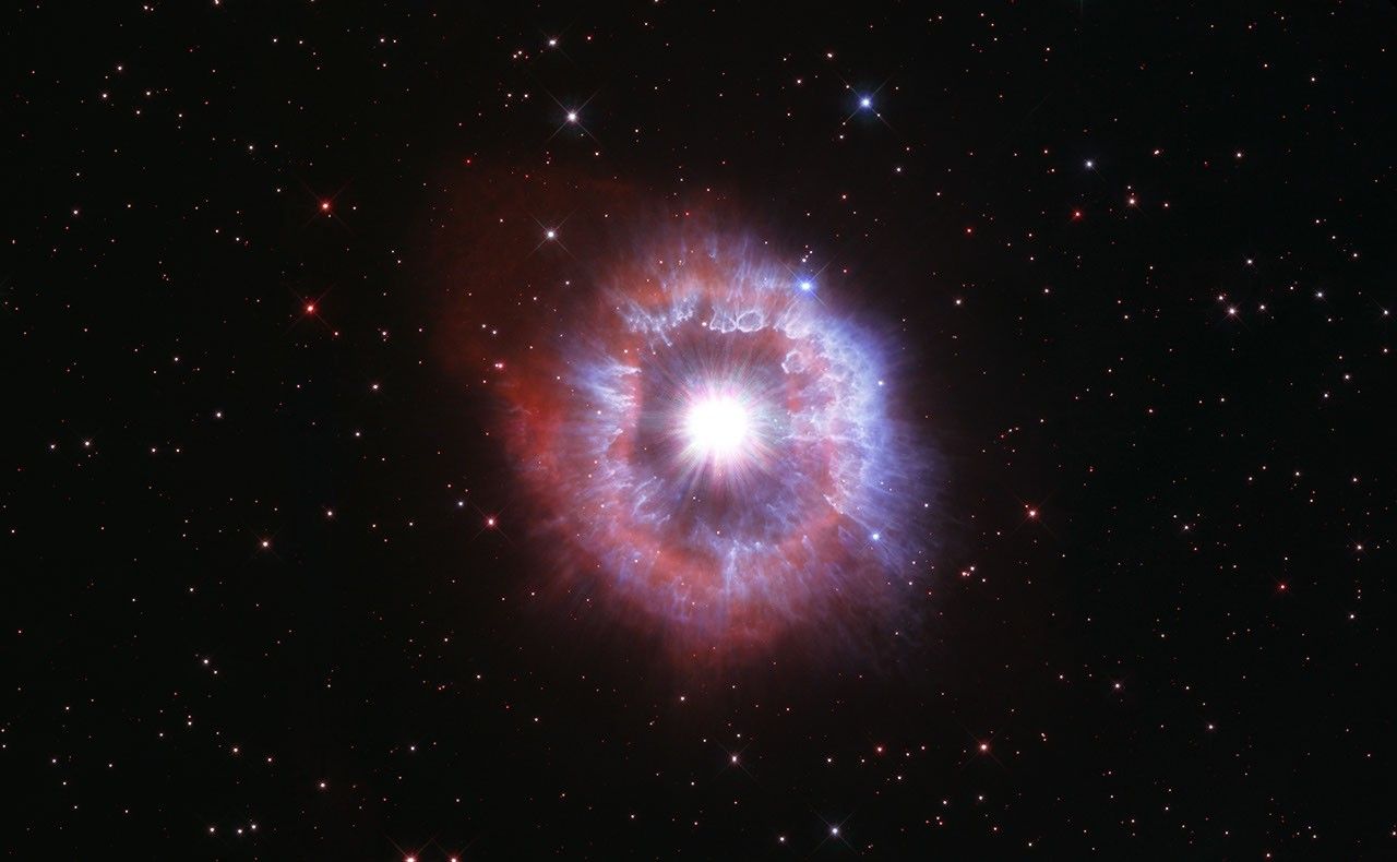 Bright star surrounded by kaleidoscopic rings of red and blue.