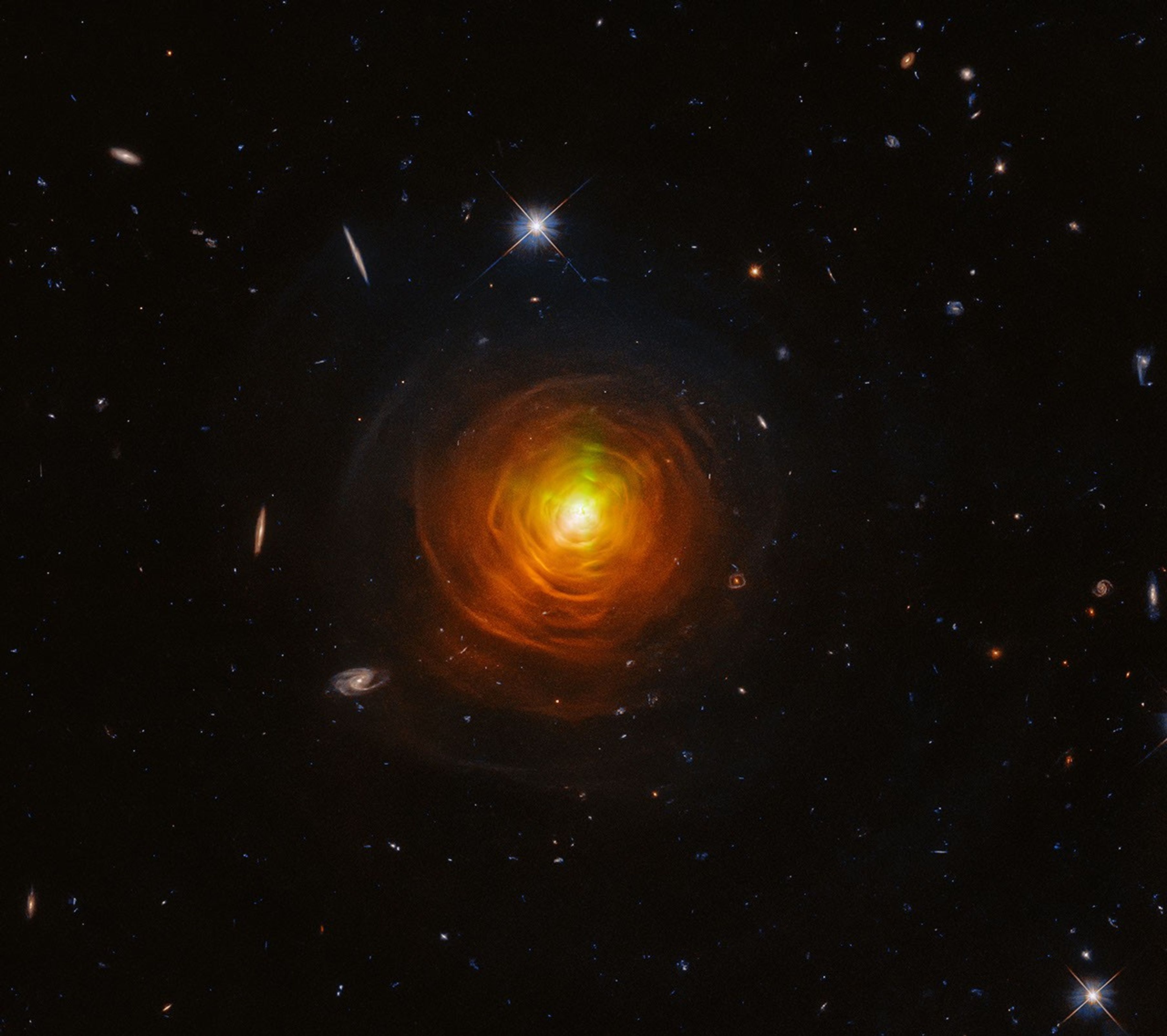 Red-orange arcs surround the carbon star CW Leonis. Brilliant searchlight beams from the star’s surface poke through.